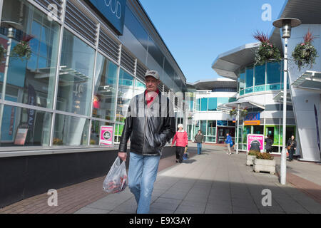 Uomo di mezza età che indossa una giacca di pelle e cappello da baseball con supporto in plastica sacco passeggiate attraverso un centro commerciale moderno. Foto Stock