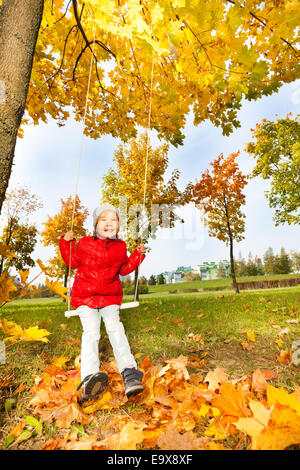 Felice ragazza siede su altalene sorridente durante l'autunno Foto Stock