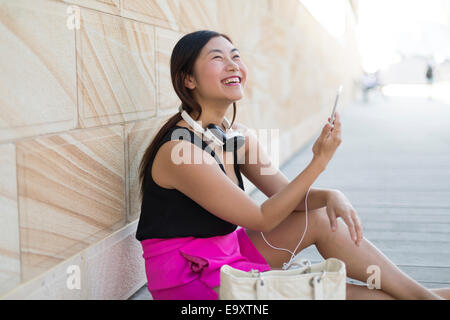 Una giovane donna rilassante utilizzando uno smartphone con le cuffie Foto Stock