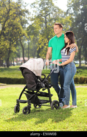 Colpo verticale di giovani genitori spingere un passeggino in un parco Foto Stock