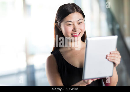 Una giovane donna asiatica utilizzando il suo tablet mentre lei è fuori e circa in ambiente urbano Foto Stock