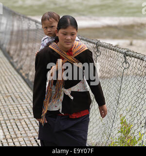 La donna che porta il suo figlio e attraversando il ponte tra la Puna Tsang River, Punakha distretto, Bhutan Foto Stock