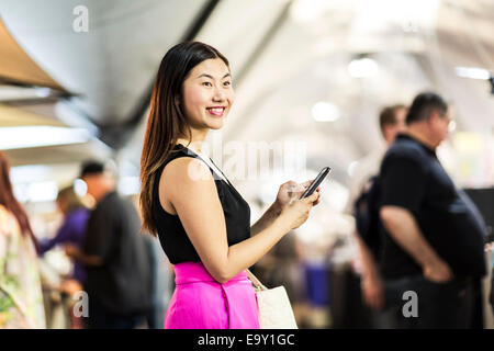 Una giovane donna asiatica utilizza il suo dispositivo mobile Foto Stock