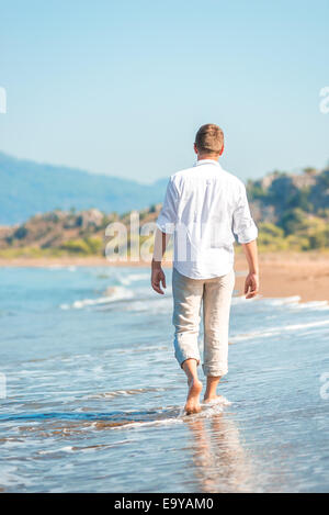 Successo giovane uomo a camminare lungo una spiaggia di sabbia Foto Stock