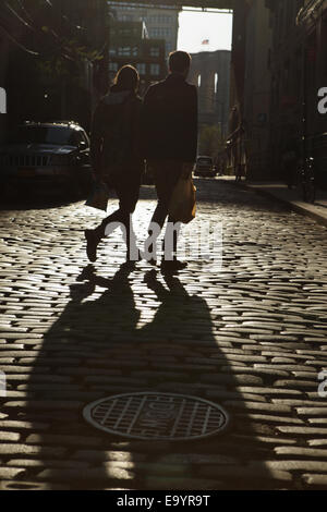 Sagome di due giovani holding hands camminando per strada di ciottoli di Brooklyn tramonto Foto Stock