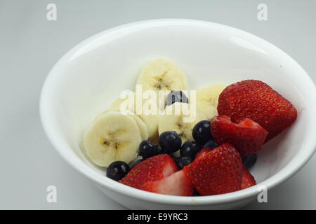 Frutta - banane, i mirtilli e le fragole in un recipiente bianco Foto Stock