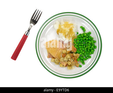 Una cotta fette di tacchino in salsa con crostoni al, purè di patate e piselli verdi su una piastra con rosso forcella gestite a lato. Foto Stock