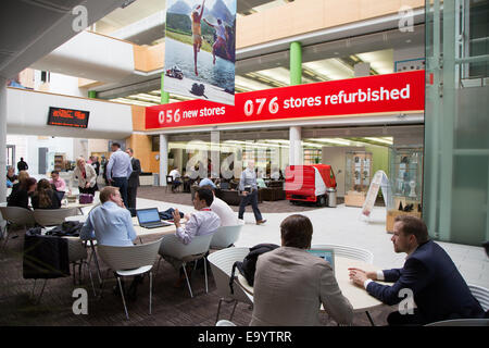 Lavoratori a bere caffè e lavorare sui dispositivi all'interno di Vodafone UK sede vicino a Newbury Foto Stock