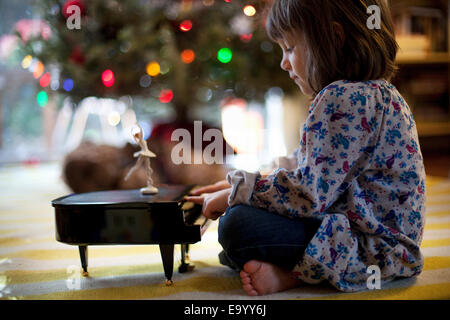 Ragazza seduta sul soggiorno piano suonare il pianoforte giocattolo music box a Xmas Foto Stock