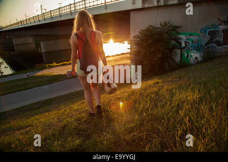 Vista posteriore del giovane donna camminare vicino a ponte e Riverside Foto Stock