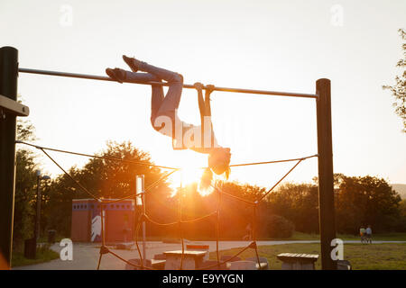Stagliano giovane donna capovolta sul parco giochi telaio arrampicata al tramonto Foto Stock
