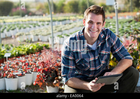 Ritratto di giovane lavoratore di sesso maschile con tavoletta digitale in vivaio polytunnel Foto Stock