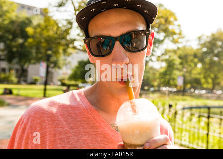 Ritratto di giovane uomo di bere frappe in posizione di parcheggio Foto Stock