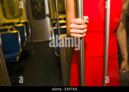Ritagliato colpo di giovane donna indossa abito rosso sul treno della metropolitana Foto Stock