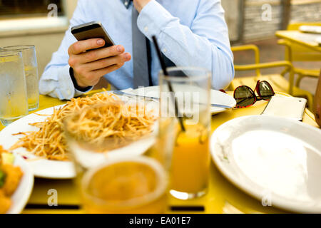 Ritagliato colpo di giovane uomo texting sullo smartphone al cafè sul marciapiede Foto Stock