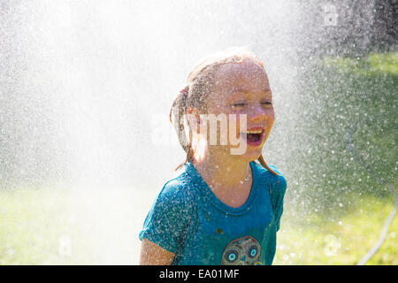Girl getting schizzato da sprinkler acqua in giardino Foto Stock