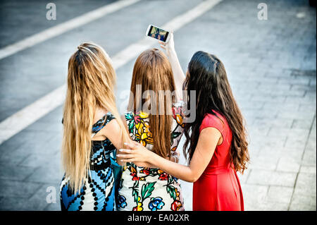 Vista posteriore di tre giovani donne tenendo selfie con lo smartphone, Cagliari, Sardegna, Italia Foto Stock