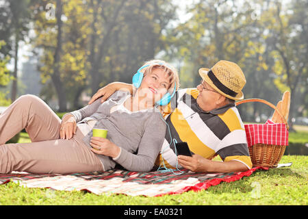 Coppia matura ascoltando musica e rilassante per un picnic nel parco in una giornata di sole Foto Stock