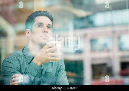 Giovane imprenditore a bere caffè e guardando fuori della finestra cafe, London, Regno Unito Foto Stock