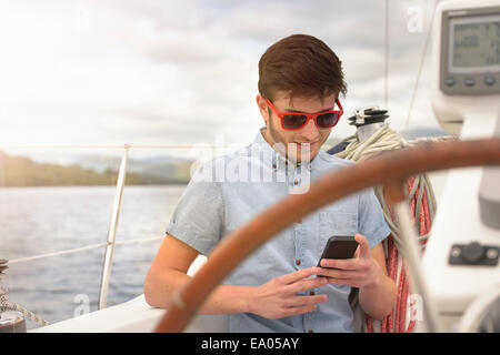 Giovane uomo utilizzando il telefono cellulare su yacht sotto il cielo sereno Foto Stock