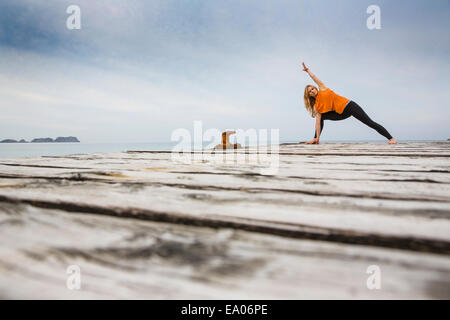 Metà donna adulta a praticare yoga posizione sul mare di legno pier Foto Stock