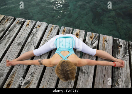 Vista aerea della metà donna adulta con le braccia e le gambe tese a praticare yoga sul mare in legno pier Foto Stock