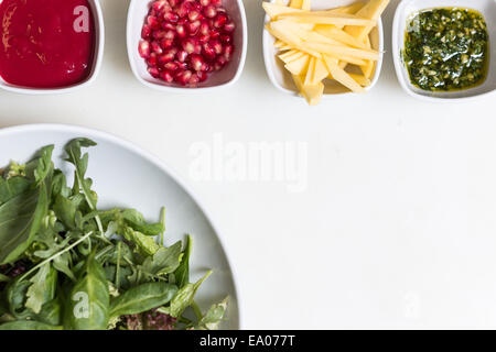 Insalata di rucola con i semi di melograno e salsa, pesto e taglio fresco avocado in ciotole su sfondo bianco Foto Stock