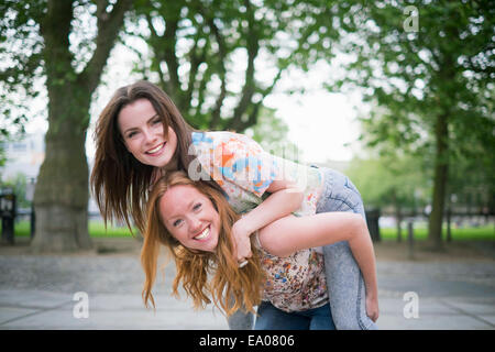 Ritratto di due giovani donne migliori amici dando piggy back in posizione di parcheggio Foto Stock