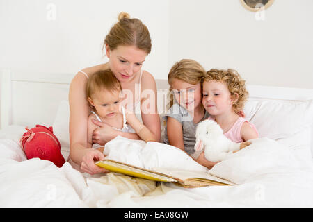 Madre libro lettura di tre figlie a letto Foto Stock