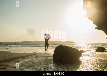Uomo maturo che corre verso il mare, holding della tavola da surf Foto Stock