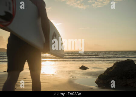 Uomo maturo, camminando verso il mare, tenendo tavola da surf Foto Stock