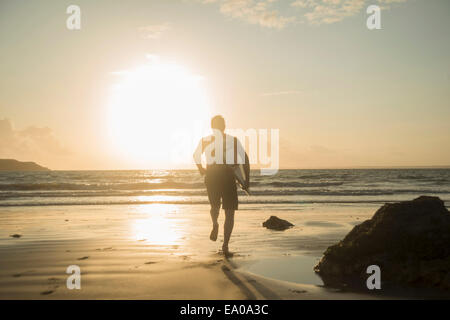 Uomo maturo, correndo verso il mare, tenendo tavola da surf Foto Stock