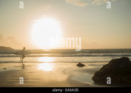 Uomo maturo, correndo verso il mare, tenendo tavola da surf Foto Stock