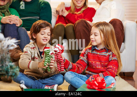 Due bambini che giocano con i regali alla vigilia di Natale e la famiglia sta a guardare Foto Stock