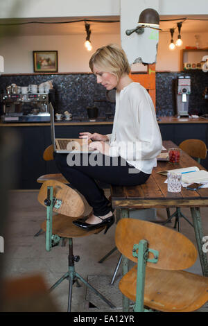 Metà donna adulta seduta sul tavolo utilizzando laptop Foto Stock