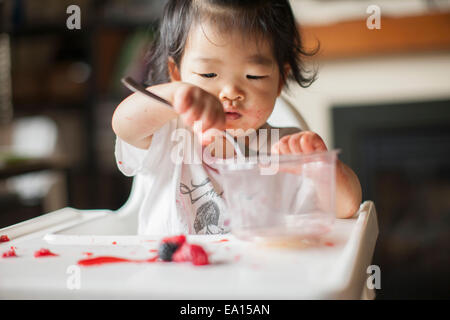 Un anno di età Baby girl mangiare la frutta nel seggiolone Foto Stock