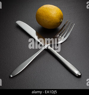 Limone attraversato con coltello e forchetta su nero Foto Stock