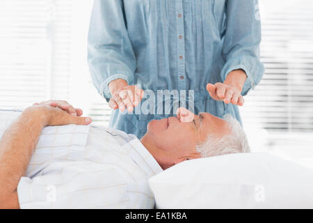 Terapista esegue Reiki oltre l'uomo senior Foto Stock