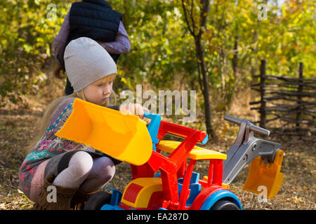 Graziosa bambina in autunno la moda gioca con colorati multicolore giocattolo di plastica di un caricatore a estremità anteriore all'aperto in giardino Foto Stock