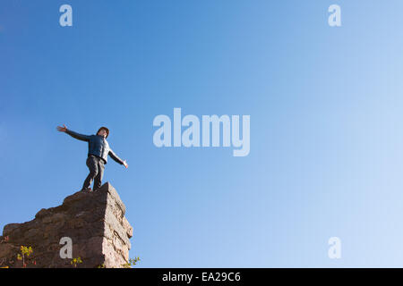 Giovane uomo celebrare in un edificio in rovina in piedi sulla cima di un alto il vecchio muro di pietra con le sue braccia distesa al sole contro un cielo blu chiaro con un sacco di copyspace, vista dal basso. Foto Stock