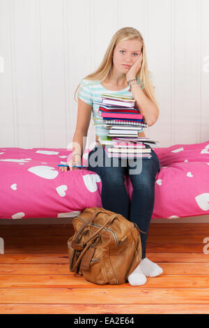 Ragazza di quattordici anni con molti libri scolastici e troppi compiti a casa Foto Stock