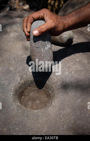 Un uomo tiene un tradizionale strumento di pietra per schiacciare il mais in Isola di Lembata, Indonesia. Foto Stock