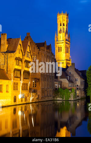 Il campanile e gli edifici illuminati di notte lungo un canale nel centro storico di Bruges, sito Patrimonio Mondiale dell'UNESCO, Belgio Foto Stock