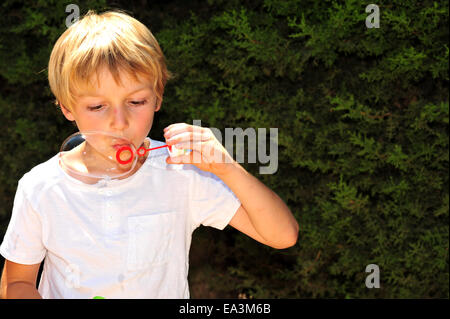 Giovane ragazzo giocando con bolle in giardino Foto Stock