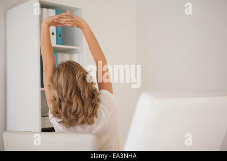 Casual imprenditrice stretching alla sua scrivania Foto Stock