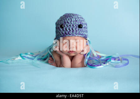 Sette giorni di età neonato bambina indossa un uncinetto meduse hat e dormire su blu tessuto a maglia. Foto Stock