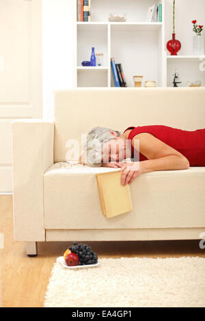 Senior donna feltro addormentato mentre la lettura sul divano nel soggiorno Foto Stock