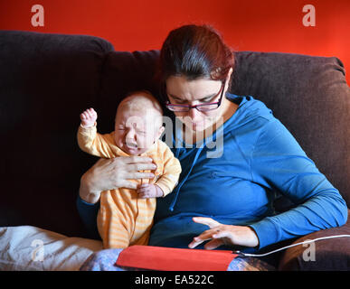 Una madre in pigiama utilizzando un ipad e ignorando la sua Gridando bambino Foto Stock