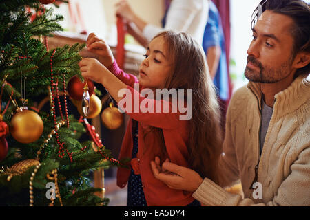 Ragazza carina la decorazione di albero di Natale con suo padre nelle vicinanze Foto Stock