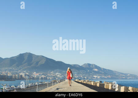 Woman in Red camminando giù pier Foto Stock